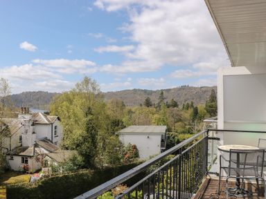 A balcony with table and chairs overlooking trees buildings and hills at The Heights in Bowness