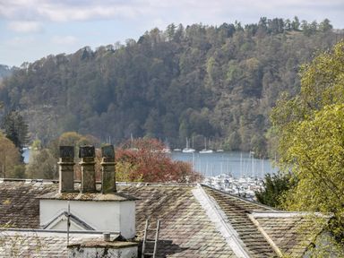 A view of rooftops with chimneys overlooking a wooded hillside and a marina with boats at The Heights in Bowness