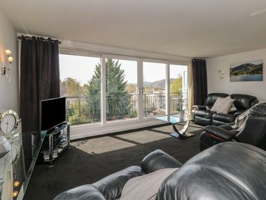 A living room with leather sofas a glass coffee table a television and large windows with a view at The Heights in Bowness