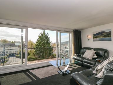 A living room with black leather sofas a glass coffee table and large sliding glass doors opening to a balcony at The Heights in Bowness