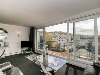 A living room with a glass coffee table leather chairs a television and large sliding glass doors opening to a balcony at The Heights in Bowness