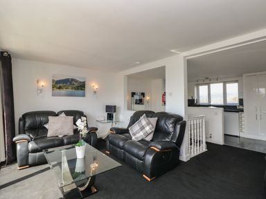 A living room with black leather sofas glass coffee table and a kitchen visible in the background at The Heights in Bowness