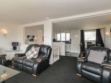 A living room with black leather armchairs and a glass side table with a lamp at The Heights in Bowness