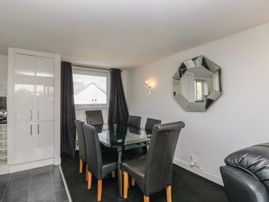 A dining area with a glass table and six black chairs near a window with dark curtains and a cabinet at The Heights in Bowness
