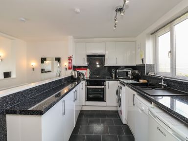 A kitchen with white cabinets black countertops a dishwasher washing machine oven toaster kettle and window at The Heights in Bowness