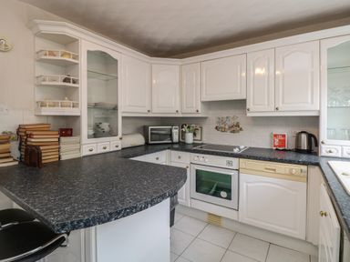 A kitchen with white cabinets black countertops an oven a microwave and stacked books at The Heights in Bowness
