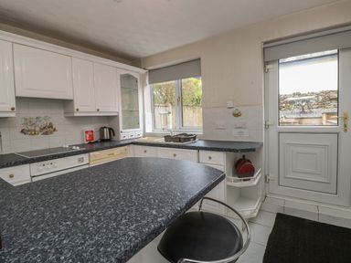 A kitchen with white cabinets a black countertop a window a door and a black chair at The Heights in Bowness