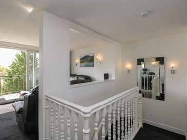 A stairway with white railing and a wall mirror beside a living area with black leather sofas at The Heights in Bowness