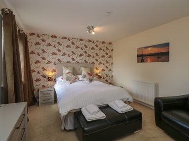 A bedroom with a double bed pillows bedside tables lamps a black bench with towels and a black armchair at The Heights in Bowness