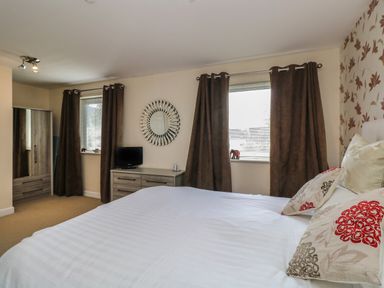A bedroom with a bed white bedding pillows dresser wardrobe two windows with brown curtains and a round mirror on the wall at The Heights in Bowness