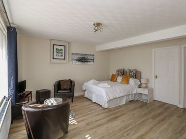 A bedroom with a double bed, two armchairs, a small TV, two paintings on the wall, and a nightstand at The Heights in Bowness