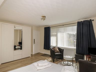 A bedroom with a bed, wardrobe with mirror, two leather chairs, small table, window with blinds and curtains at The Heights in Bowness