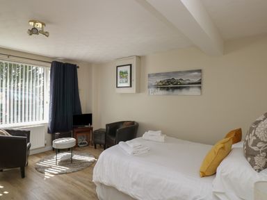 A bedroom with a bed chairs a small table a television and windows with curtains at The Heights in Bowness