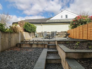 A multi-level backyard with gravel areas a garden bed stone steps and outdoor table and chairs at The Heights in Bowness