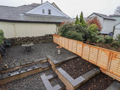 A backyard with gravel ground and garden beds separated by a wooden fence and stone wall at The Heights in Bowness