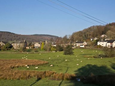 A rural landscape with sheep grazing on a green field and houses near trees and hills at Cherry Tree Cottage at Satterthwaite in Hawkshead