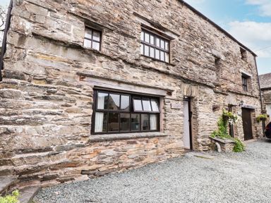 Stone exterior wall of a cottage with windows doors and gravel driveway at Cherry Tree Cottage at Satterthwaite in Hawkshead