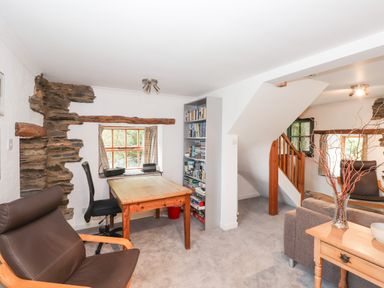 A room with a wooden table and chairs stone wall accents and a bookshelf near a staircase at Cherry Tree Cottage at Satterthwaite in Hawkshead