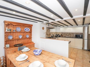 A kitchen and dining area with wooden table set for four and cabinets with kitchen appliances at Cherry Tree Cottage at Satterthwaite Hawkshead