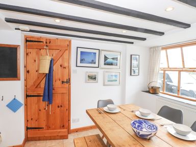 A dining area with wooden table and chairs next to a window and a wooden door with pictures on the wall at Cherry Tree Cottage at Satterthwaite Hawkshead