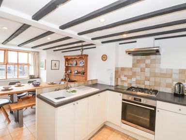 A kitchen with a sink, gas stove, oven, kettle, wooden dining table with chairs and a wooden cabinet with blue and white dishes at Cherry Tree Cottage at Satterthwaite in Hawkshead