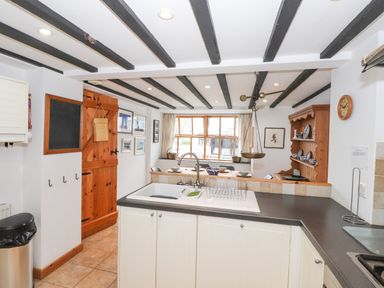 A kitchen with a sink and countertop looking into a dining area with a wooden cabinet and window at Cherry Tree Cottage at Satterthwaite in Hawkshead