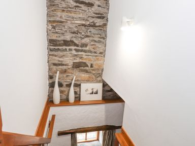 A stairwell with a stone wall and two tall white vases and a framed picture on a wooden ledge at Cherry Tree Cottage at Satterthwaite Hawkshead