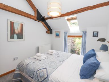 A bedroom with a bed covered in a patterned quilt and blue pillows under a skylight window with curtains at Cherry Tree Cottage at Satterthwaite in Hawkshead