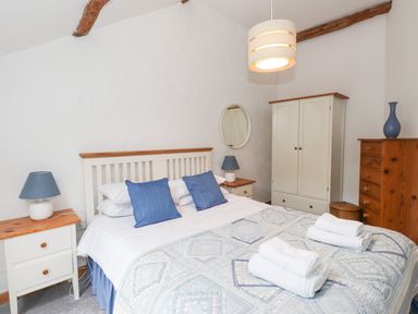 A bedroom with a double bed two bedside tables with lamps a wardrobe a chest of drawers and folded towels on the bed at Cherry Tree Cottage at Satterthwaite Hawkshead