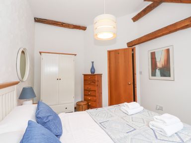 A bedroom with a bed with blue pillows white wardrobe wooden dresser and wooden beams on ceiling at Cherry Tree Cottage at Satterthwaite in Hawkshead