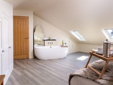 A bathroom with a freestanding bathtub wooden door sloped ceiling and skylights at Old Wool Loft in Ambleside
