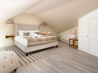 A bedroom with a bed a striped rug lamps a small wooden table and a white wardrobe at Old Wool Loft in Ambleside