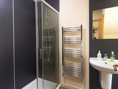 A bathroom with a glass shower enclosure a chrome towel rack a white sink with toiletries and a mirror at Old Wool Loft Ambleside