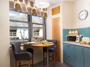 A kitchen corner with a round wooden table set for two and blue cabinets at Old Wool Loft in Ambleside