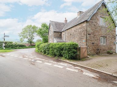 A stone house with hedges and a wooden gate beside a road with a signpost at Home Farm House in Penrith