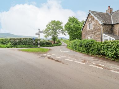 A rural road intersection with a stone house and hedges along the roads at Home Farm House in Penrith