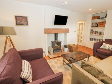 A living room with sofas a coffee table a fireplace with a mounted television and a bookshelf at Home Farm House in Penrith