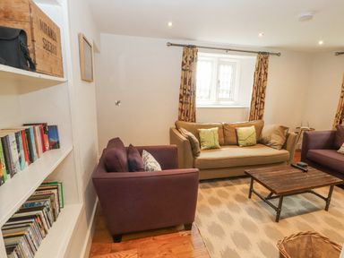 A sitting room with two purple armchairs a brown sofa a wooden coffee table bookshelves and a window with patterned curtains at Home Farm House Penrith