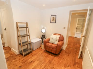 A small room with a leather armchair pillows a tripod lamp a ladder shelf a white storage box and wooden floor at Home Farm House in Penrith