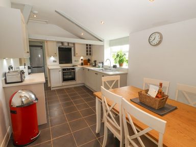 A kitchen with a wooden dining table and white chairs next to a window with a plant at Home Farm House in Penrith