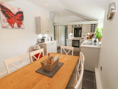 A kitchen with white cabinets a wooden dining table with white chairs and a red butterfly painting on the wall at Home Farm House in Penrith