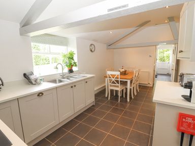 A kitchen with a sink under a window a dining table with chairs and kitchen appliances at Home Farm House in Penrith