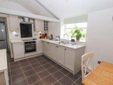 A kitchen with cabinets a stove a sink window with plants and a wooden table with a chair at Home Farm House Penrith