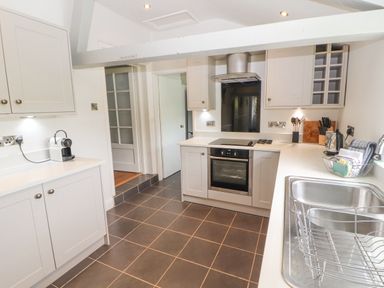 A kitchen with cabinets a stove oven a sink a dish drying rack and a coffee machine at Home Farm House in Penrith