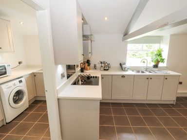 A kitchen with gray cabinets a stovetop a kettle a sink a drying rack and a washing machine at Home Farm House in Penrith