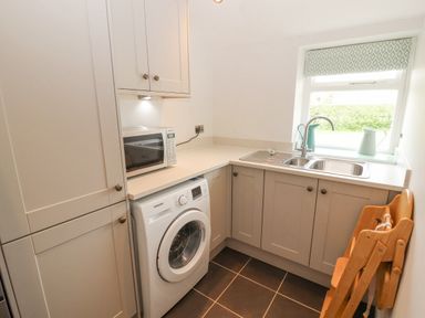A utility room with a washing machine microwave cabinets sink and a wooden high chair at Home Farm House Penrith