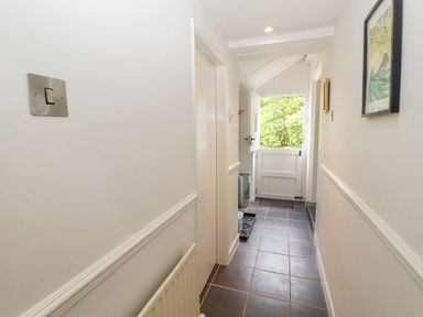 A narrow hallway with tiled floor a white door open to outside and framed pictures on the walls at Home Farm House in Penrith