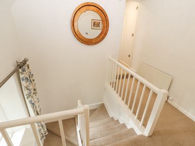 A staircase with beige carpet white railing a round wooden mirror and floral curtains at Home Farm House in Penrith