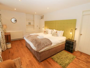 A bedroom with a large bed with green headboard bedside tables lamps a wooden floor and a small green rug at Home Farm House in Penrith