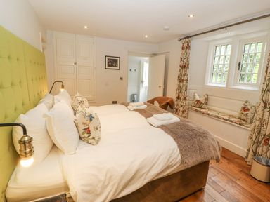 A bedroom with a large bed with white bedding and patterned cushions by a window seat at Home Farm House in Penrith